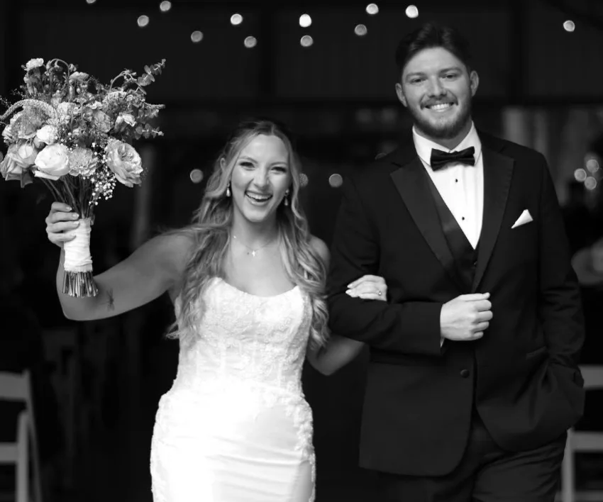 A bride and groom walking out together, smiling, in black and white
